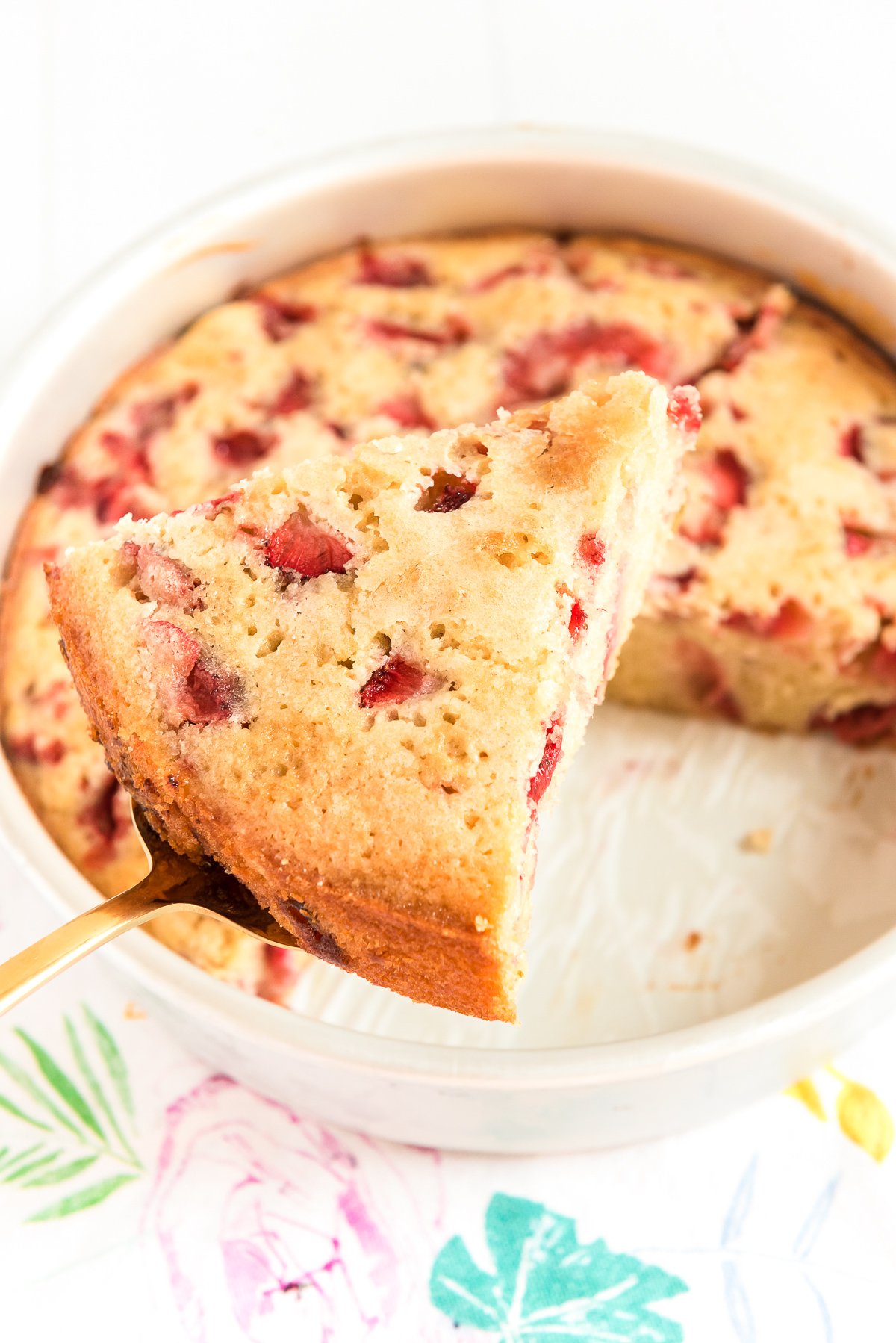 Slice of strawberry cake on a cake serving being removed from cake pan.