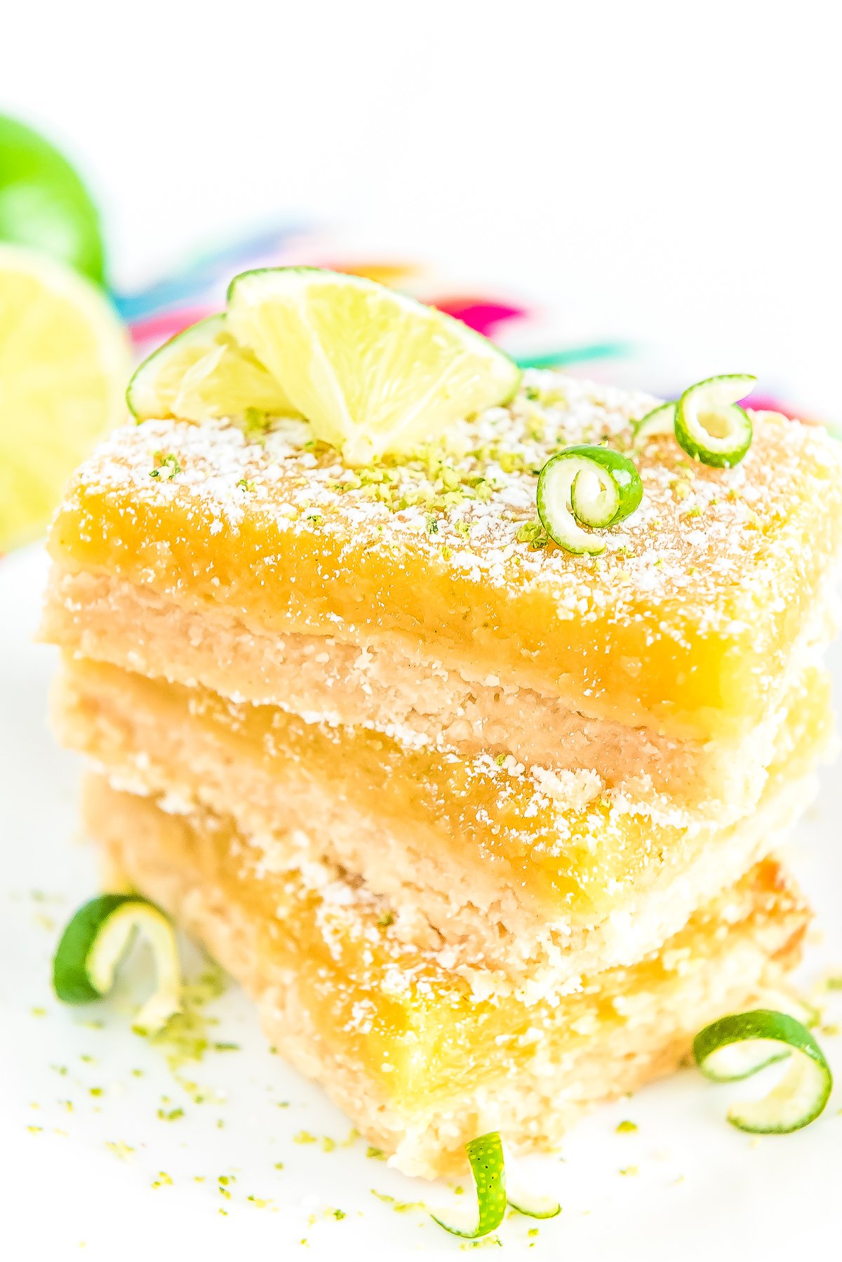 Stack of Key Lime Bars on a white plate garnished with powdered sugar and lime zest.