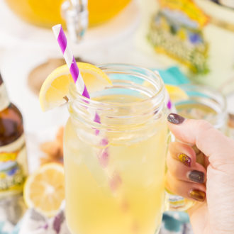 Woman's hand holding a lemonade shandy in a handled mason jar.