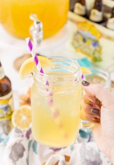 Woman's hand holding a lemonade shandy in a handled mason jar.