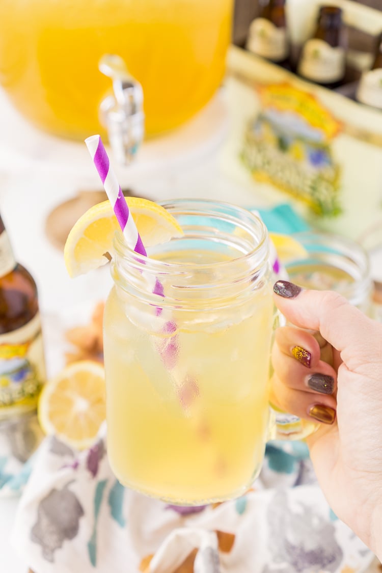 Woman's hand holding a lemonade shandy in a handled mason jar.