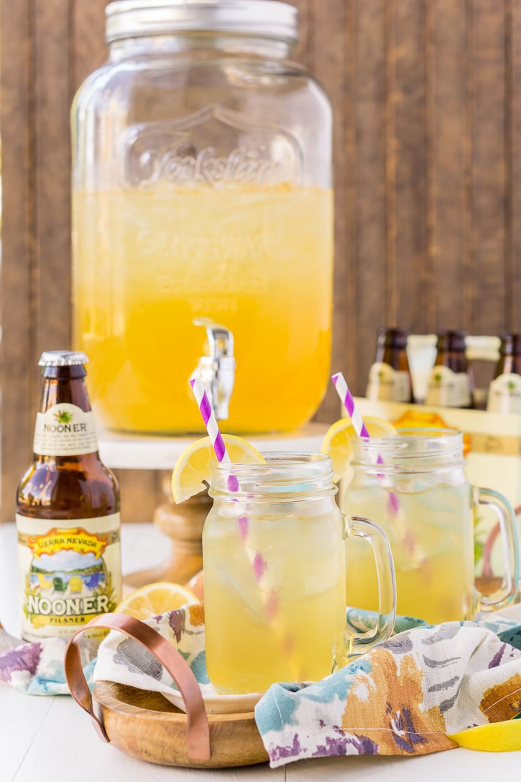 Mason jars filled with a shandy cocktail in front of a drink dispenser and beer bottles.