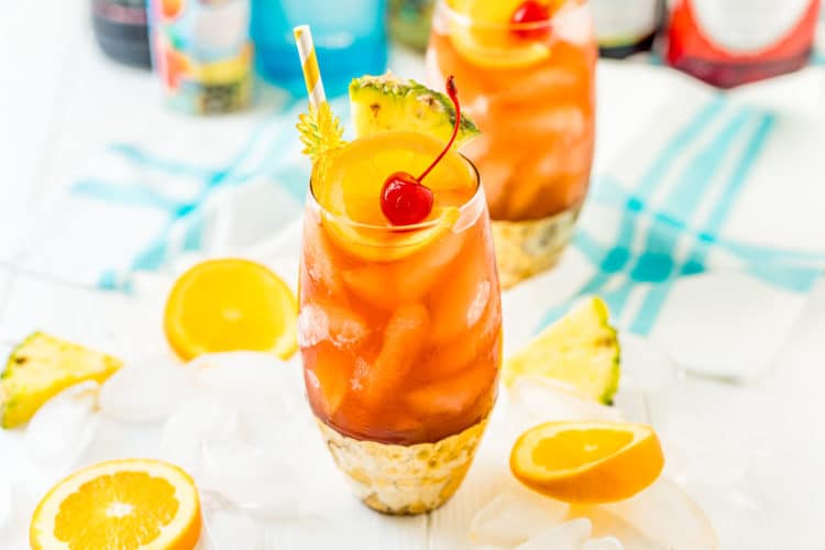 Rum Runner cocktail on a white table with slices of fruit and ice cubes scattered around it.