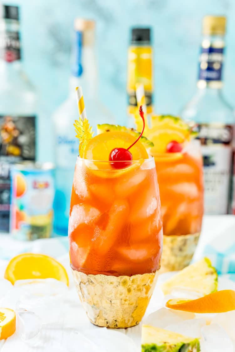 Photo of a rum runner cocktail with another drink and bottles of liqueur behind it.