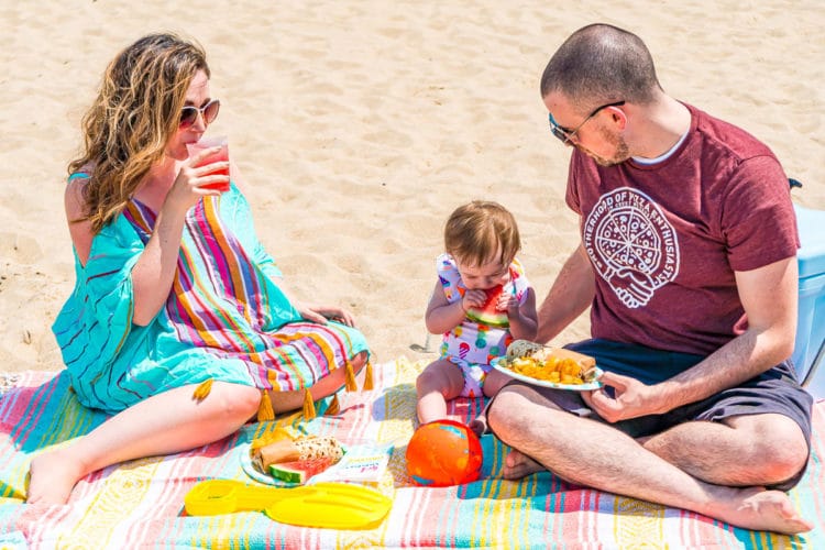 Family of three enjoying a picnic on the beach in the summer.