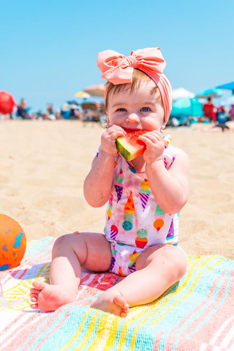 Baby girl eating watermelon at the beach.