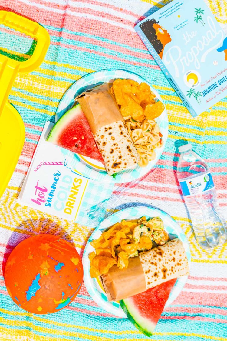 Beach picnic spread with food, napkins, books, and beach toys.