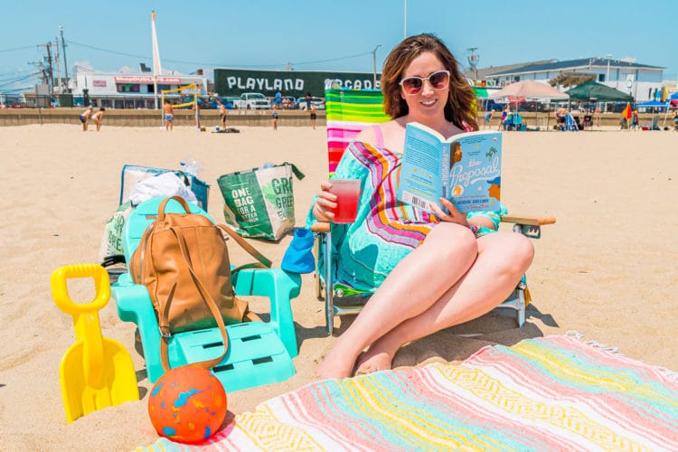 Woman sitting in a beach chair reading and drinking a lemonade.