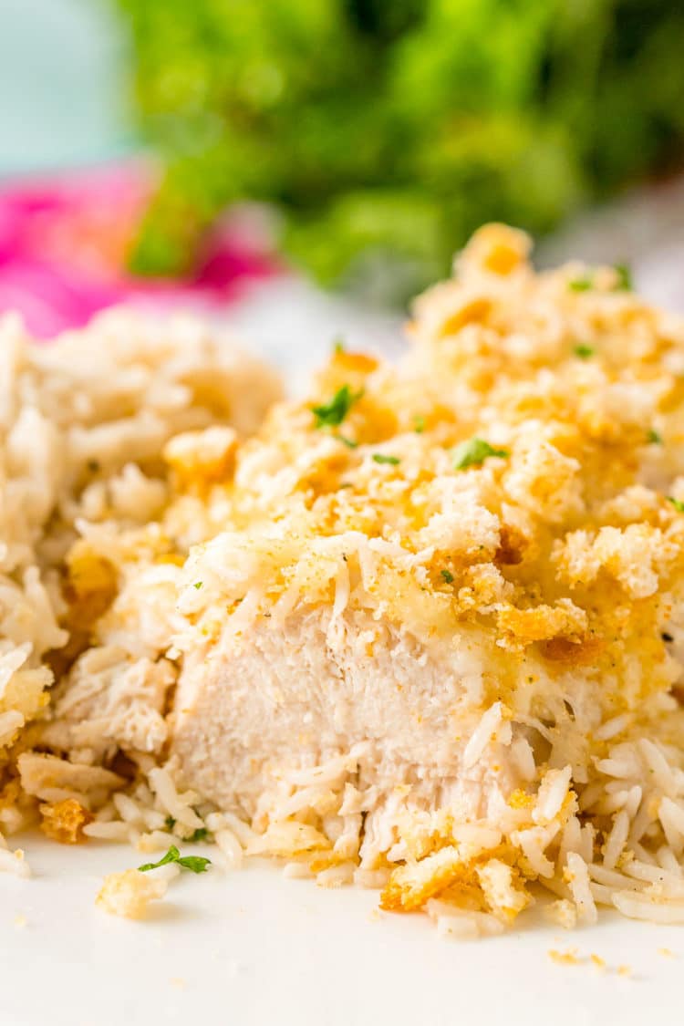 Close up photo of a baked chicken breast that has been cut into. Crusted with croutons and served with rice.