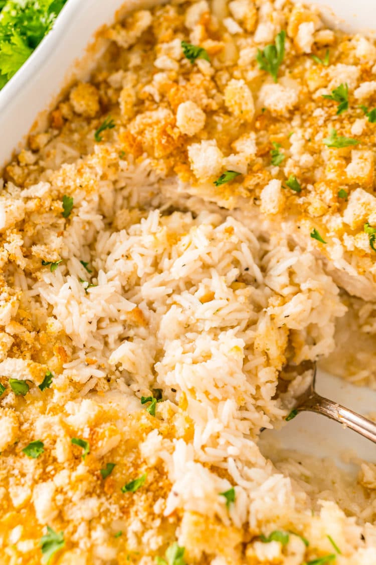 Rice being spooned out of a white casserole dish.