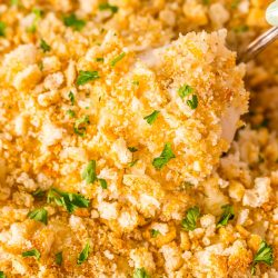 Close up photo of a chicken breast being scooped out of a chicken and rice casserole.