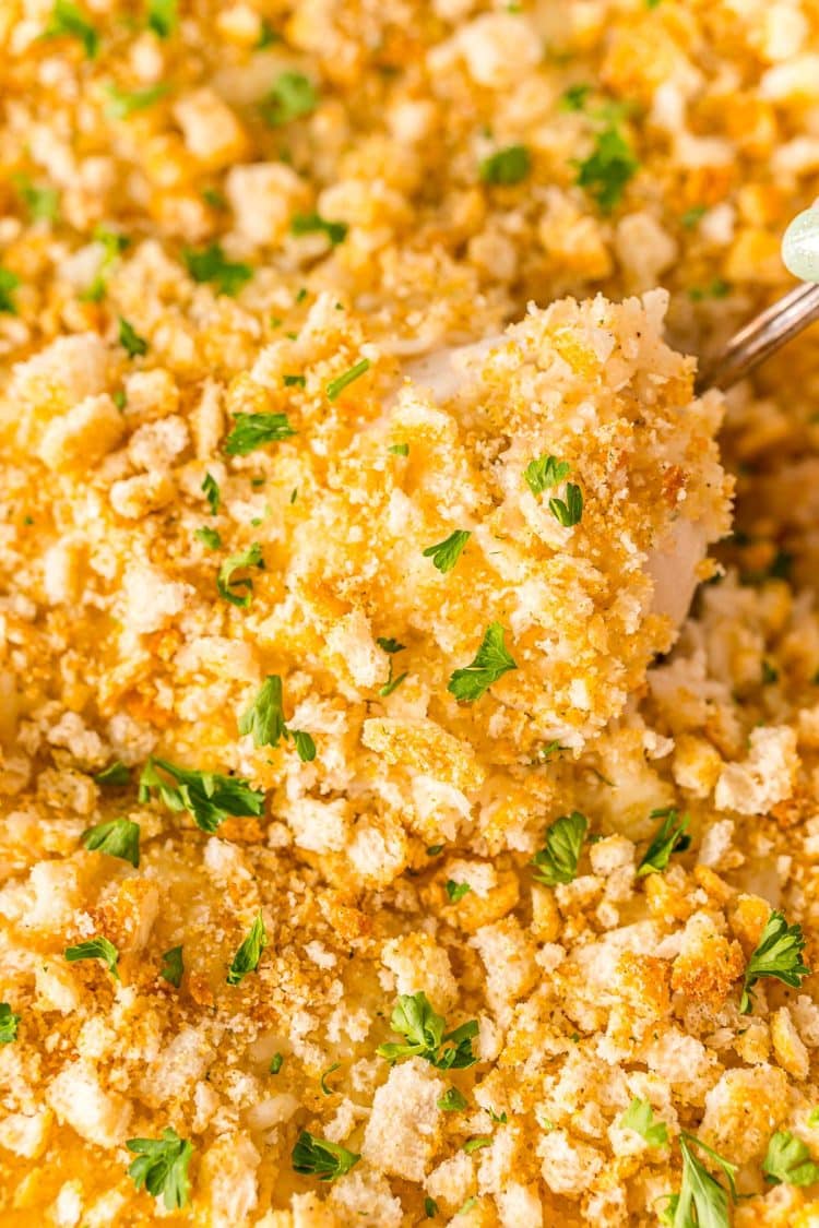 Close up photo of a chicken breast being scooped out of a chicken and rice casserole.