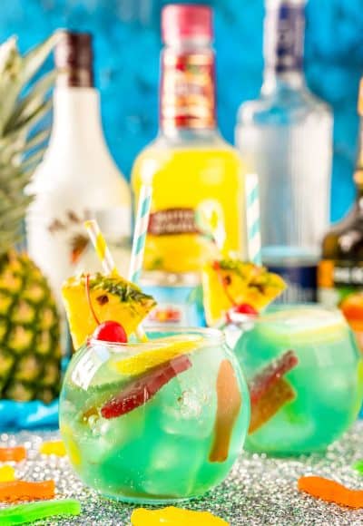 Fish bowl cocktail with pineapple and bottles of alcohol in the background.