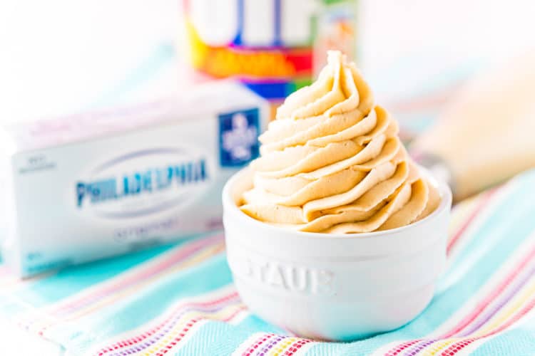 photo of peanut butter frosting in a white bowl with a block of cream cheese and jar of peanut butter in the background.