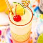Close up photo of a pineapple daiquiri garnished with a maraschino cherry, lime wedge, and gold straw.