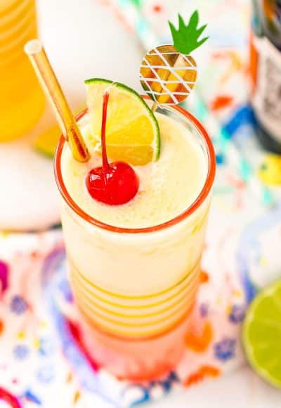 Close up photo of a pineapple daiquiri garnished with a maraschino cherry, lime wedge, and gold straw.