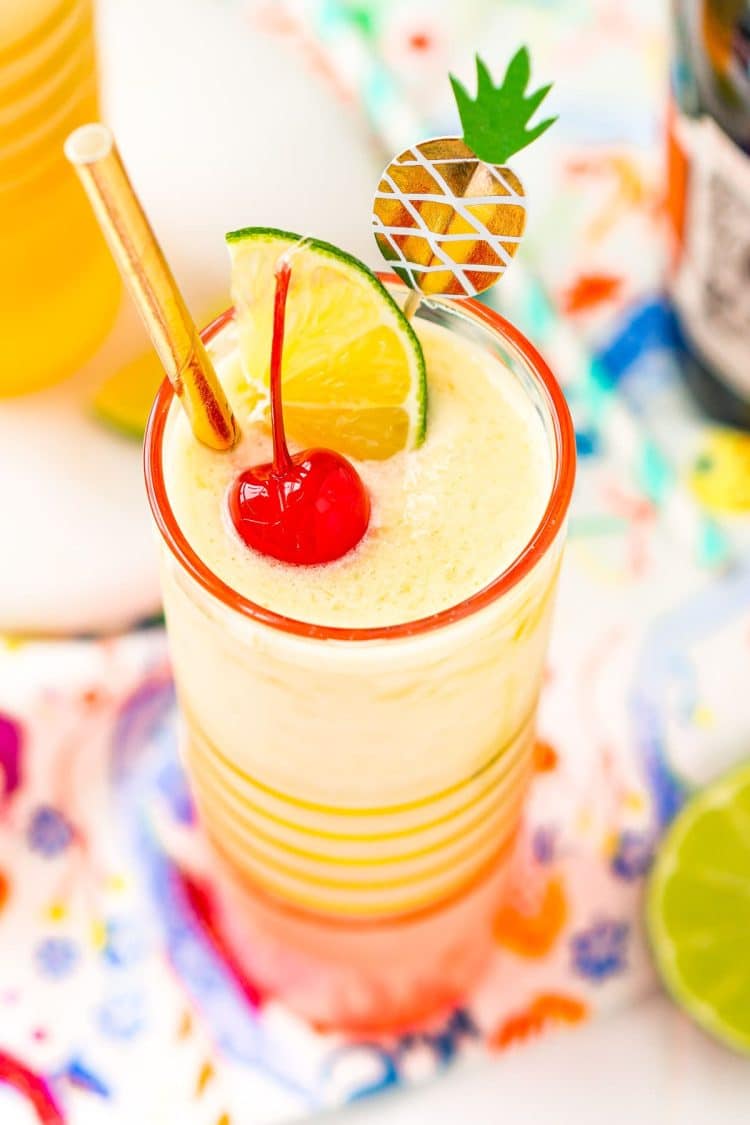 Close up photo of a pineapple daiquiri garnished with a maraschino cherry, lime wedge, and gold straw.