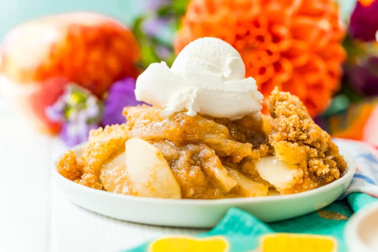 Photo of a serving of brown betty on a white plate with colorful flowers in the background.