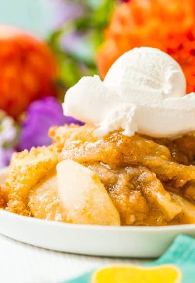 Close up photo of apple brown betty on a white plate topped with ice cream.