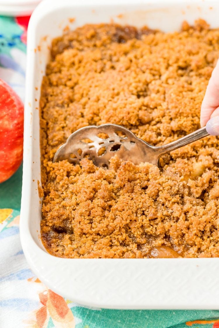 Woman's hand scooping apple brown betty out of a baking dish.