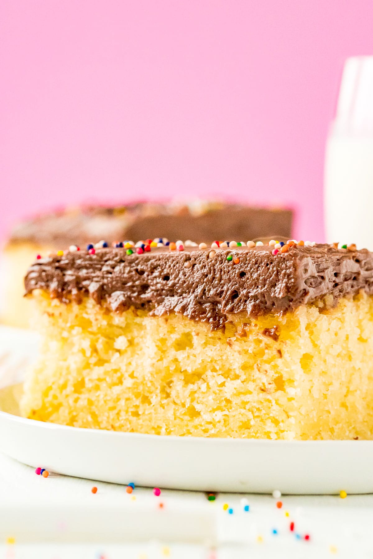 Slice of yellow sheet cake with chocolate frosting on a white plate.