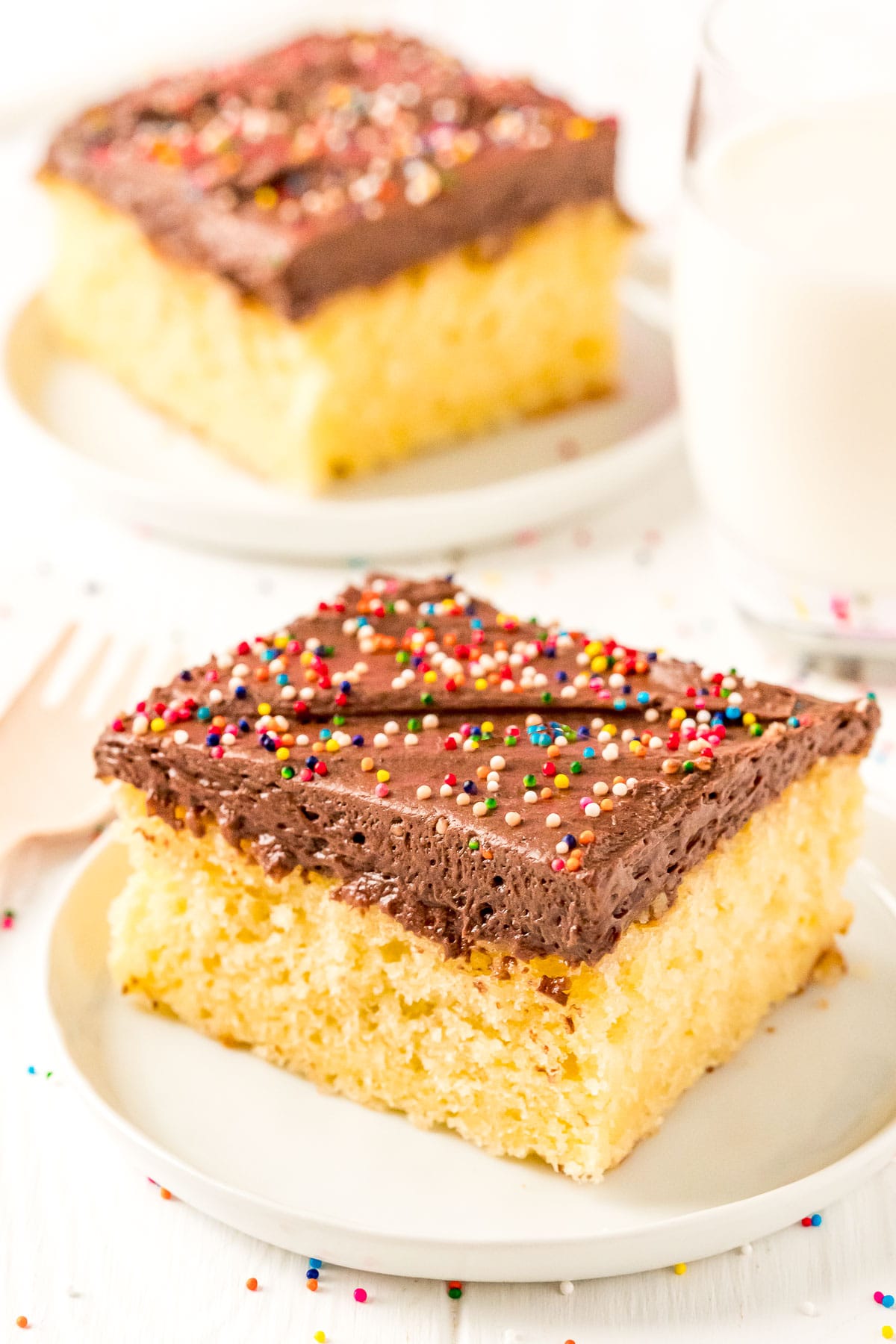 Slices of yellow cake on small white plates with a glass of milk.