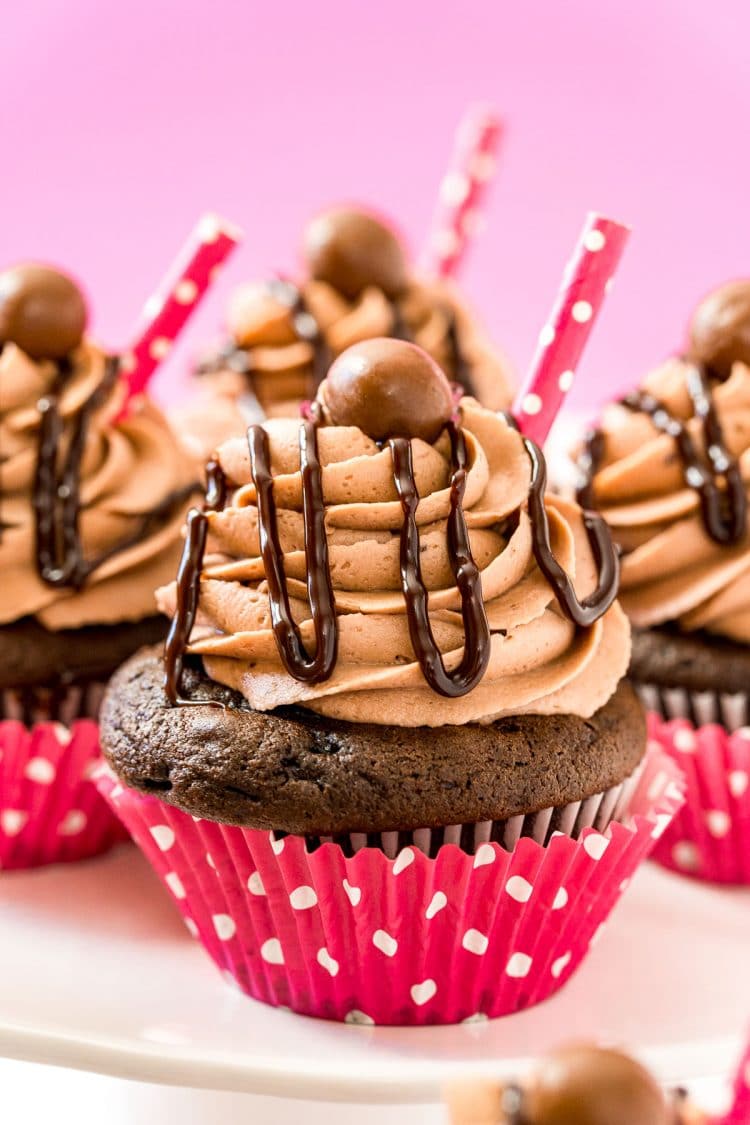 Chocolate cupcakes in pink wrappers with chocolate sauce drizzled over the frosting.