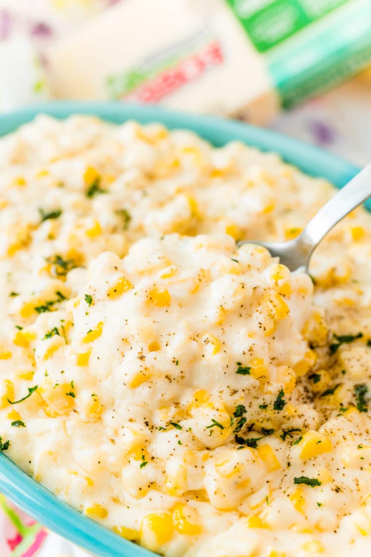 A serving spoon scooping cheesy corn out of a dish.