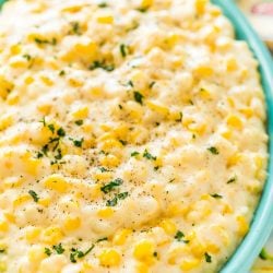 Close up photo of a teal serving dish filled with cheesy corn.