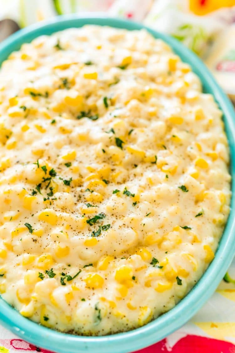 Close up photo of a teal serving dish filled with cheesy corn.