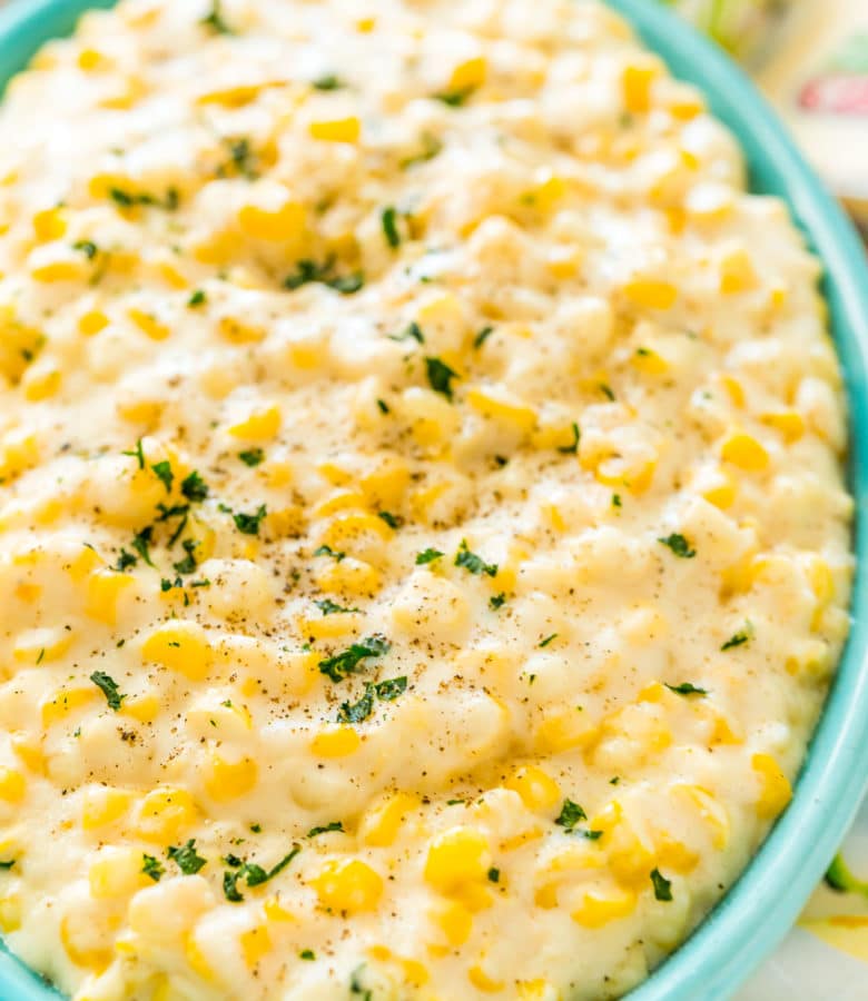 Close up photo of a teal serving dish filled with cheesy corn.