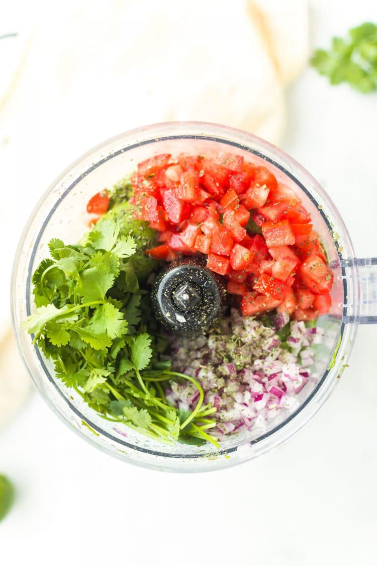 Herbs, onions, and tomatoes in a food processor.