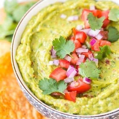 Close up photo of a bowl of guacamole garnished with diced tomatoes, cilantro, and red onion.