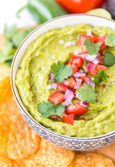 Close up photo of a bowl of guacamole garnished with diced tomatoes, cilantro, and red onion.