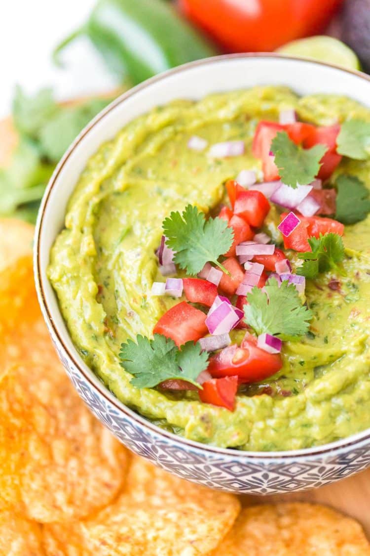 Close up photo of a bowl of guacamole garnished with diced tomatoes, cilantro, and red onion.