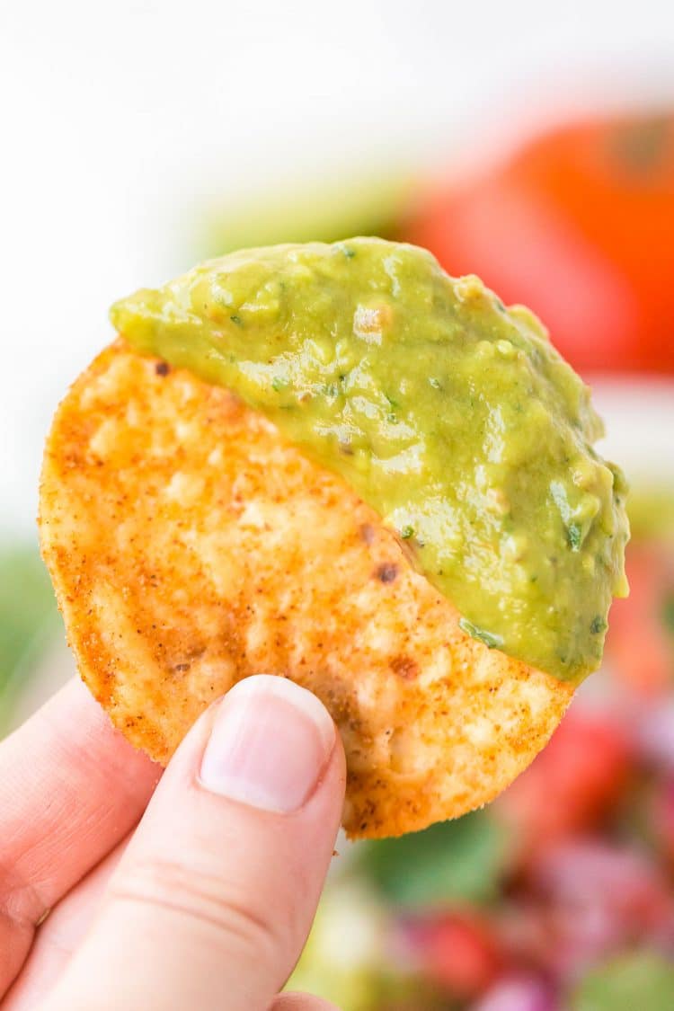 Woman's hand holding a tortilla chip that's been dipped in guacamole.