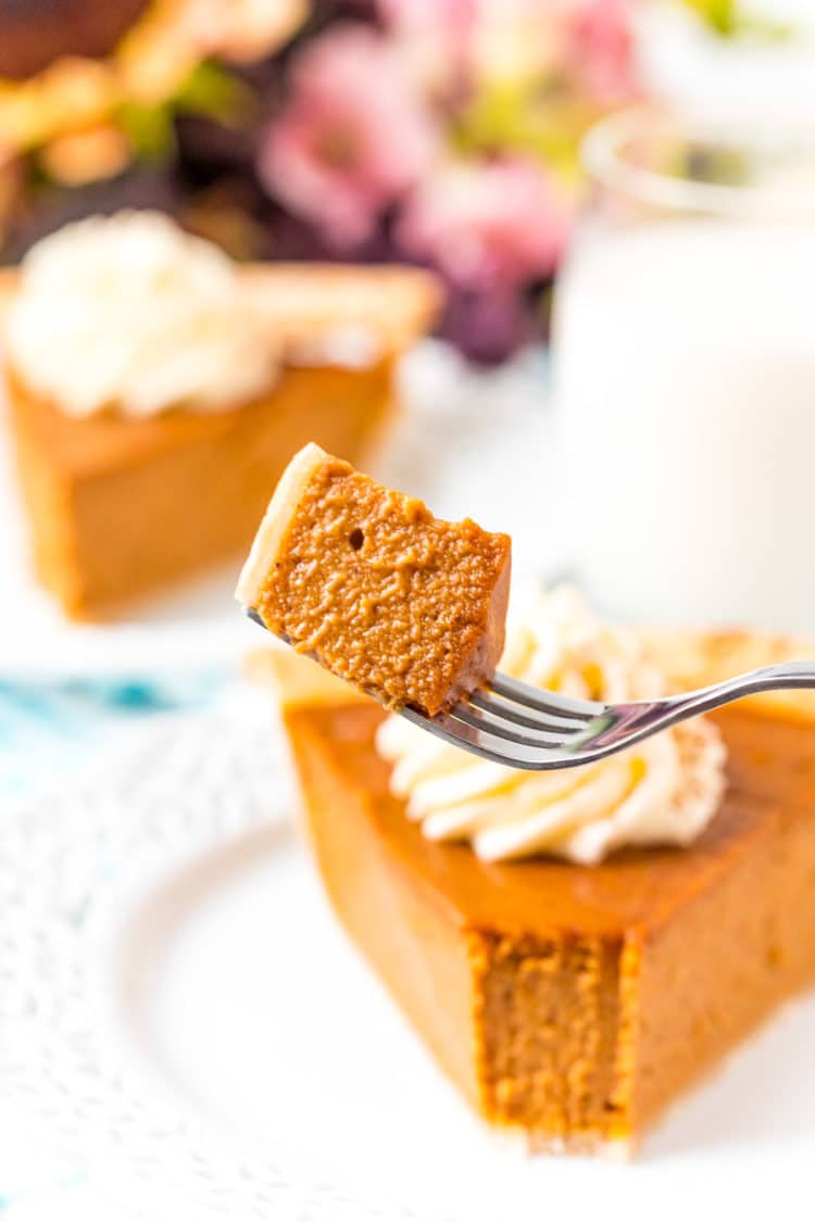 Bite of pumpkin pie on a fork with slices of pie in the background.