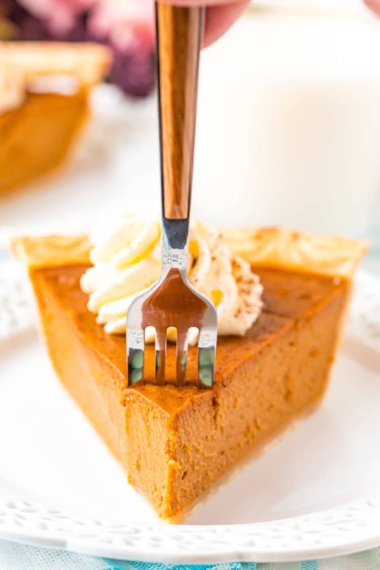 A fork taking a bite out of a slice of pumpkin pie.