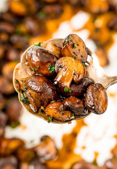 Serving spoon filled with sauteed mushrooms.