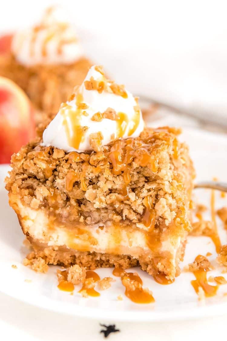 Square slice of apple cheesecake bar with caramel drizzle on a white plate.