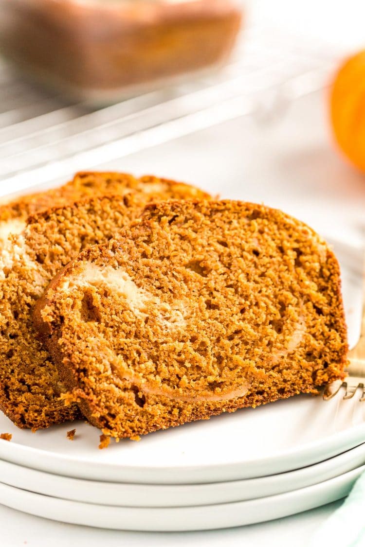 Close up photo of two slices of pumpkin bread with a cream cheese swirl on a white plate.