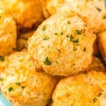 Close up photo of a bowl of cheddar drop biscuits topped with herbs.