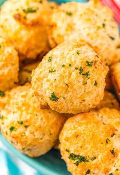 Close up photo of a bowl of cheddar drop biscuits topped with herbs.