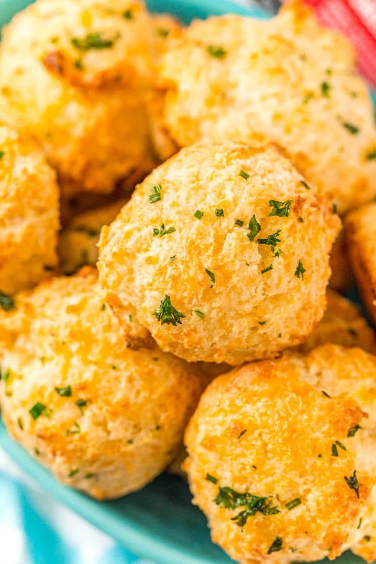 Close up photo of a bowl of cheddar drop biscuits topped with herbs.