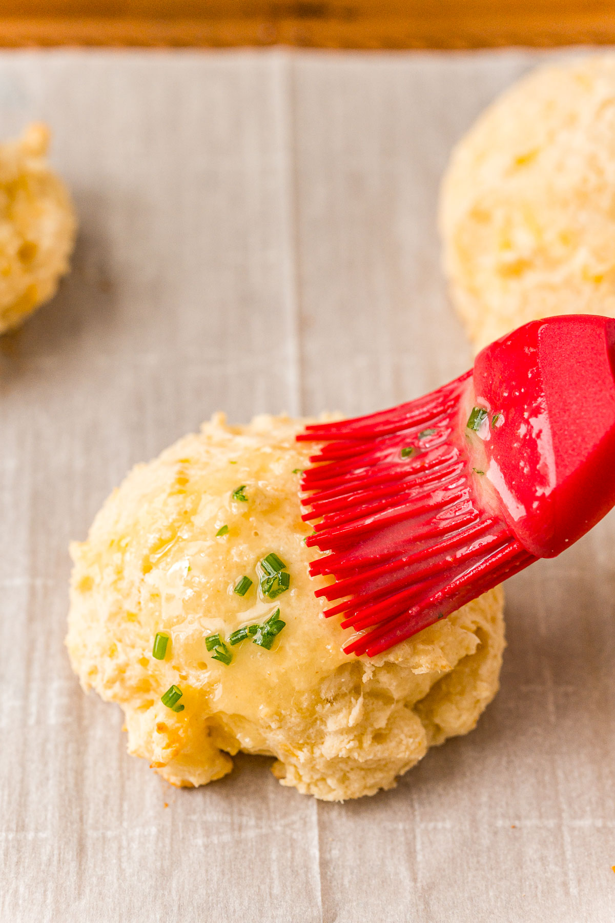 A pastry brush brushing butter on a biscuit.