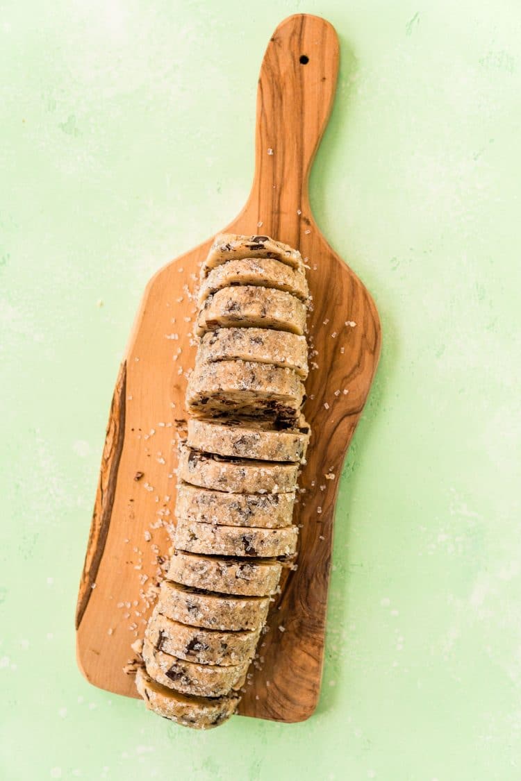 Log of cookie dough that has been sliced for baking on a cutting board.