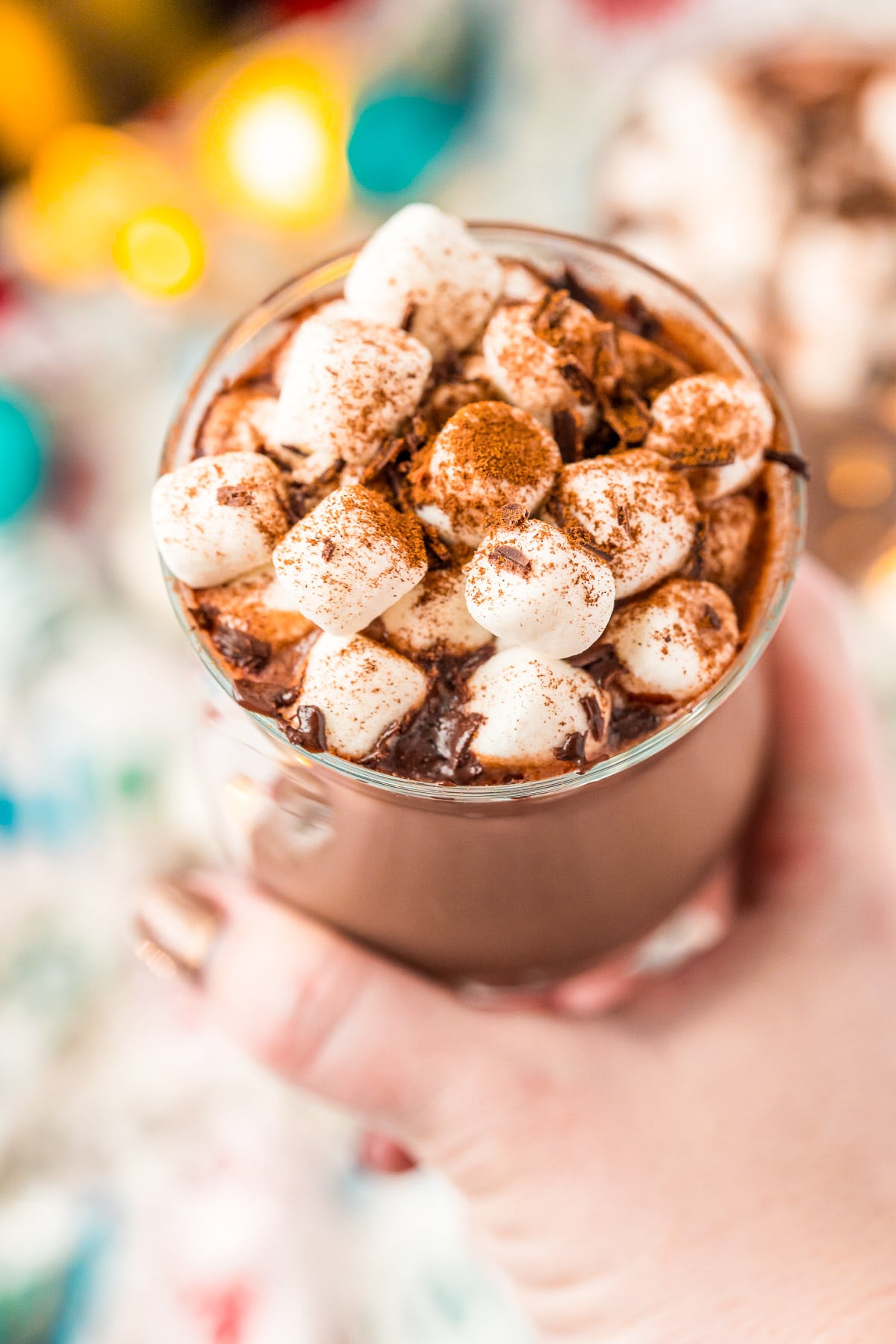 Woman's hand holding a mug of hot chocolate topped with marshmallows and cinnamon.