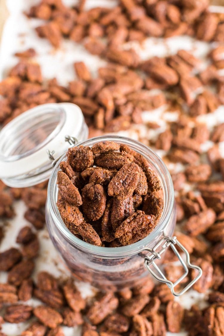 Candied pecans in a glass jar with pecans scattered around.