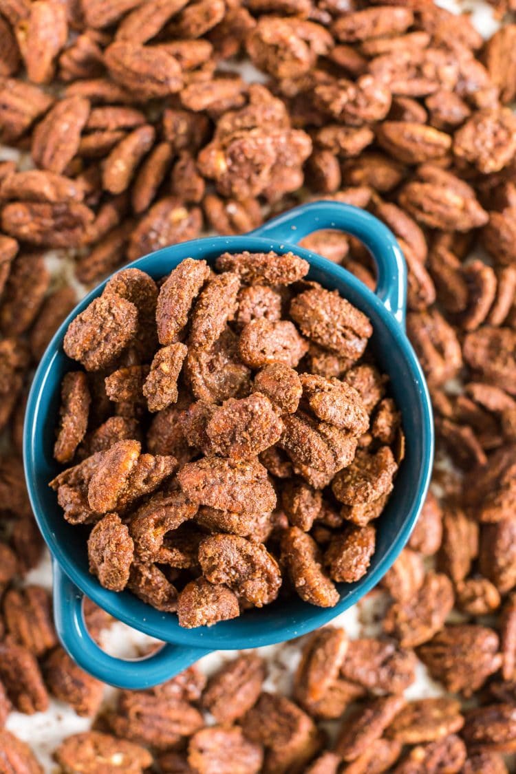 overhead photo of a blue bowl with candied pecans in it and scattered around.