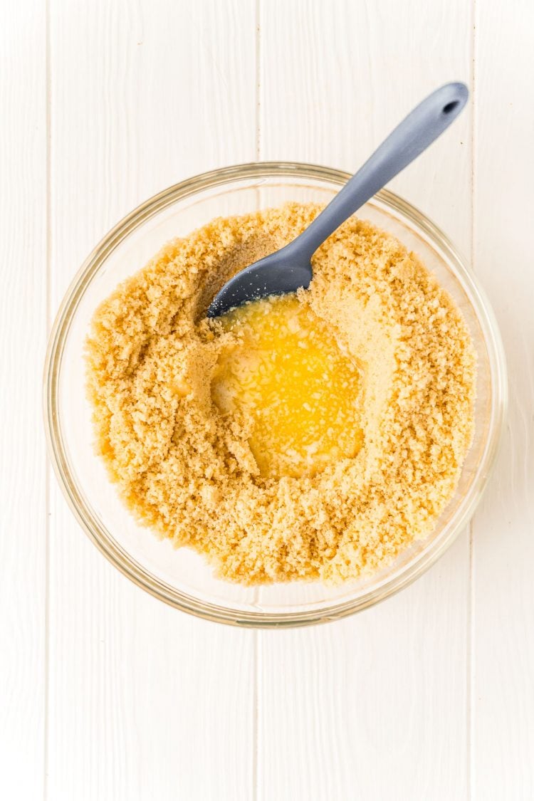 Cookie crumbs in a bowl with melted butter and a mixing spoon.